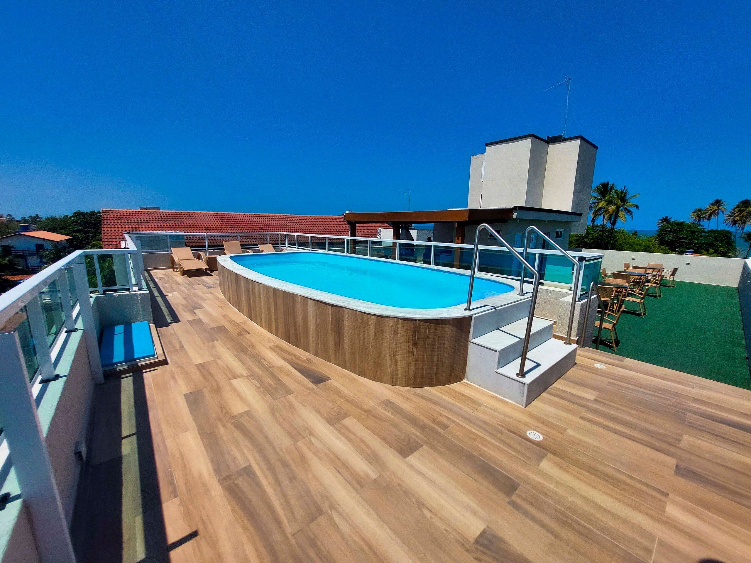 Ein Pool auf dem Dach mit Holzterrasse, Glasgeländer und einer Sitzgelegenheit im Freien.