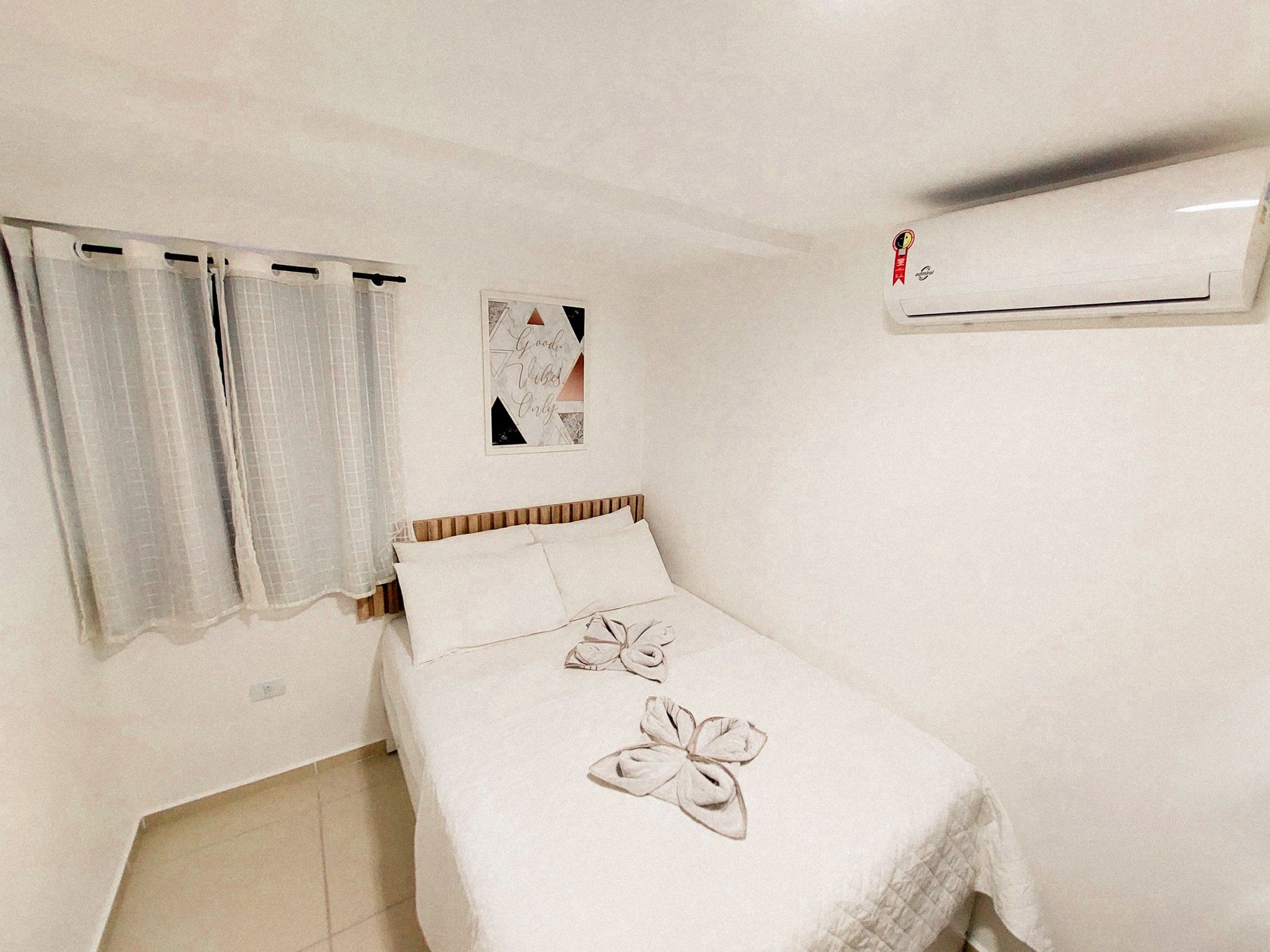 A bedroom with a bed, curtains, a wall-mounted air conditioner, and a framed picture.