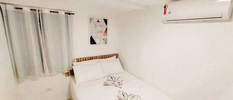 A bedroom with a bed, curtains, a wall-mounted air conditioner, and a framed picture.