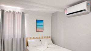 A hotel room with a bed, white curtains, a painting of a beach, and an air conditioning unit. - Residencial Engenheiro Paulo Borba (Ipojuca)