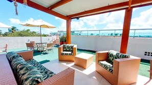 A rooftop terrace with wicker furniture, a table, and chairs, overlooking a cityscape. - Residencial Engenheiro Paulo Borba (Ipojuca)