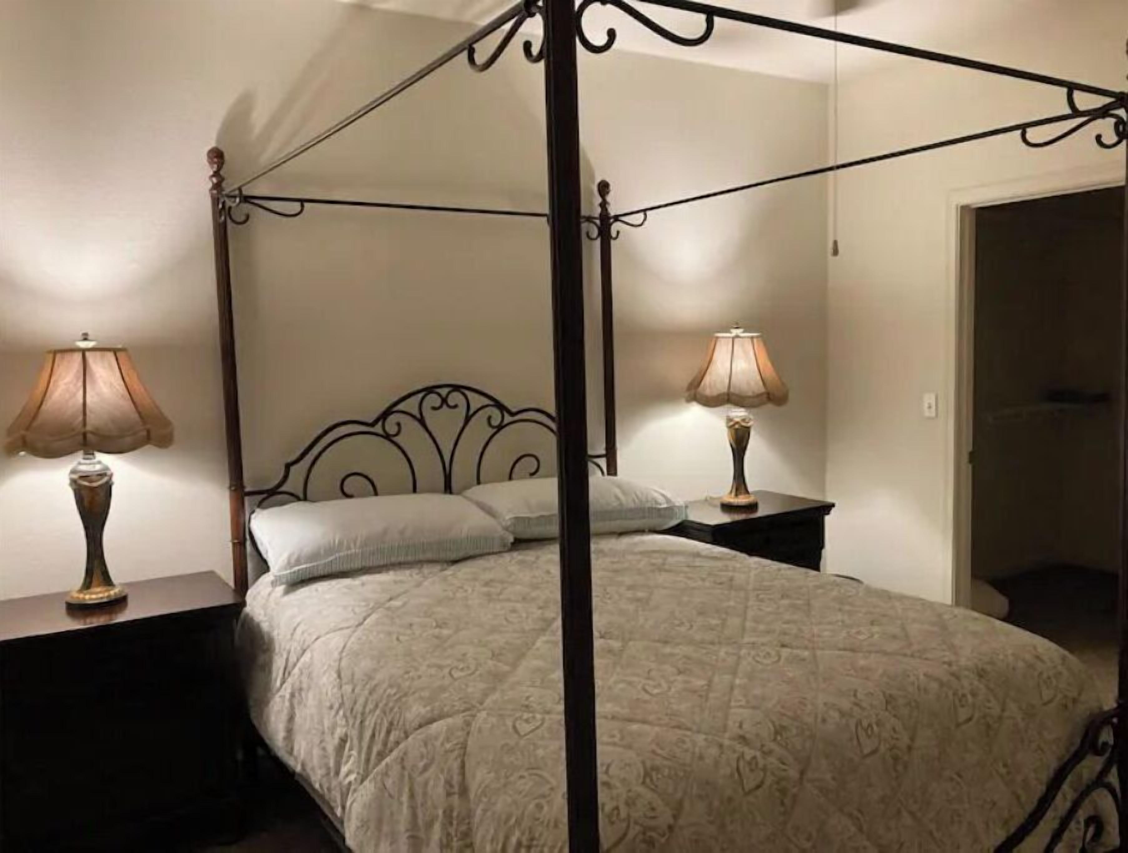A four-poster bed with a patterned bedspread, two bedside lamps, and a dark wooden headboard.
