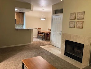 Una sala de estar con chimenea, un comedor con mesa y sillas, y una cocina con mostrador y fregadero.