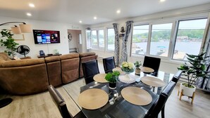 A modern living room with a brown leather sofa, a dining table with placemats, and a TV displaying streaming services.