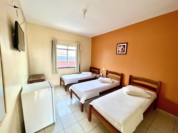 A hotel room with two single beds, a desk, a chair, a television, and a window with curtains.