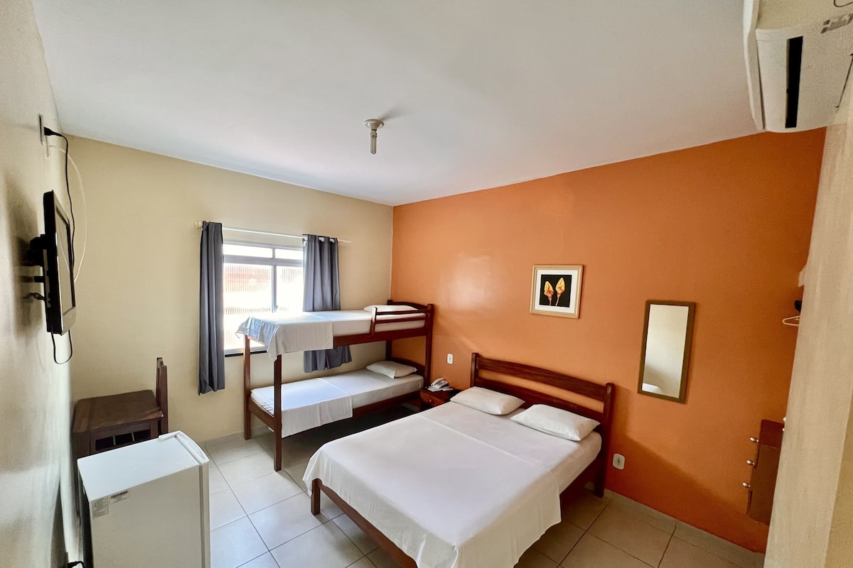 Ein Zimmer mit einem Etagenbett, einem Schreibtisch, einem Stuhl, einem kleinen Kühlschrank und einem Fenster mit Vorhängen.