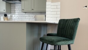 A kitchen with a green bar stool, wooden herringbone flooring, and pendant lighting.