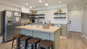 Uma cozinha moderna com ilha central, banquetas, frigorífico, micro-ondas e forno embutido.