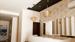 A modern reception area with a white reception desk, a large mirror, and two pendant lights. - ML Studio (Tulum)