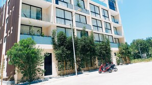 A multi-story hotel with balconies, large windows, and a parking area with motorcycles. - ML Studio (Tulum)