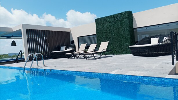 A rooftop pool area with a clear blue pool, lounge chairs, and a modern building with a green hedge. - ML Studio (Tulum)