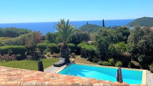 Una piscina con vista al océano, rodeada de exuberante vegetación y un techo de tejas.