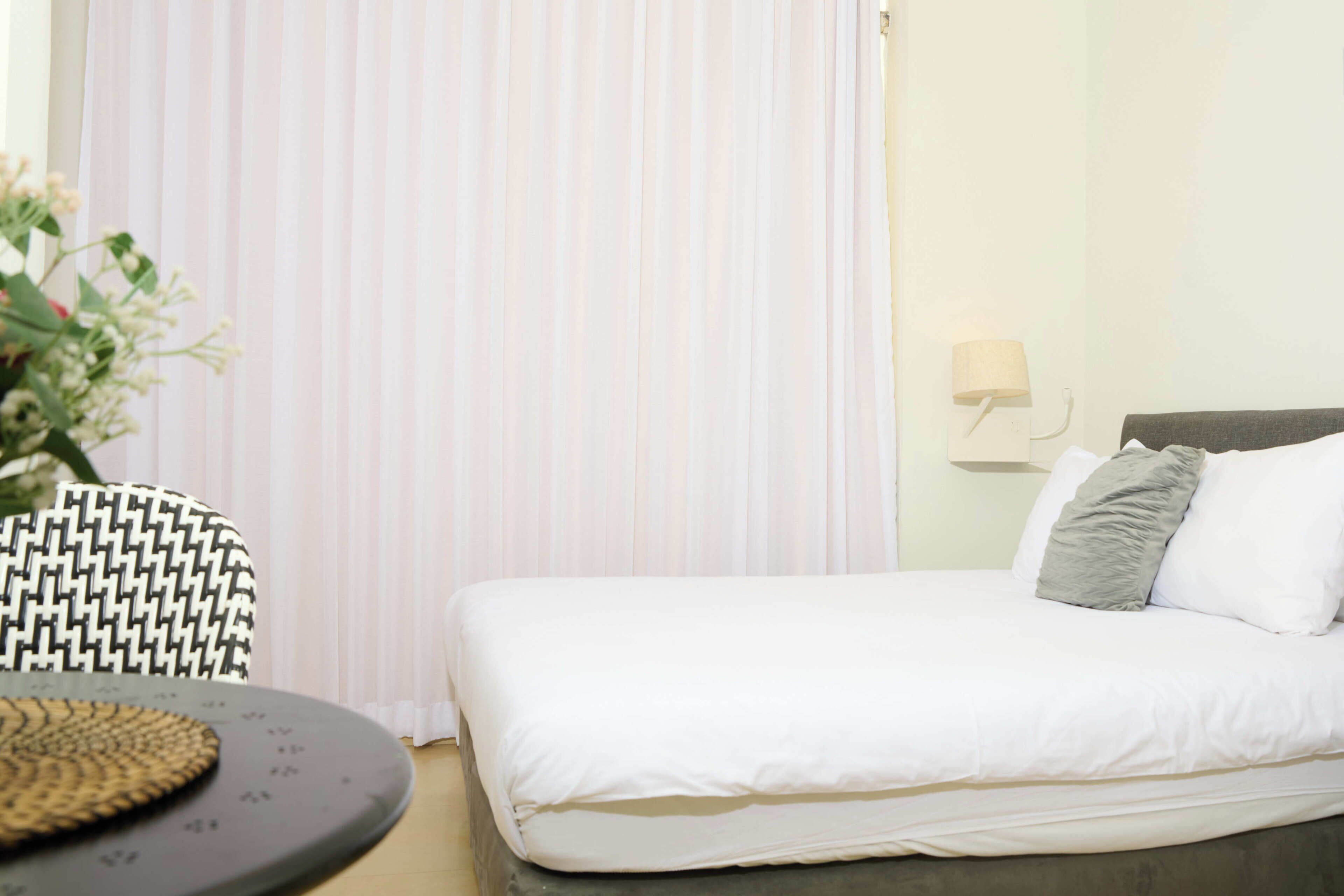 Una habitación de hotel con una cama, una silla, una lámpara y una planta.
