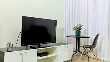 A flat-screen TV on a white cabinet, a small table with a plant, and a black chair.