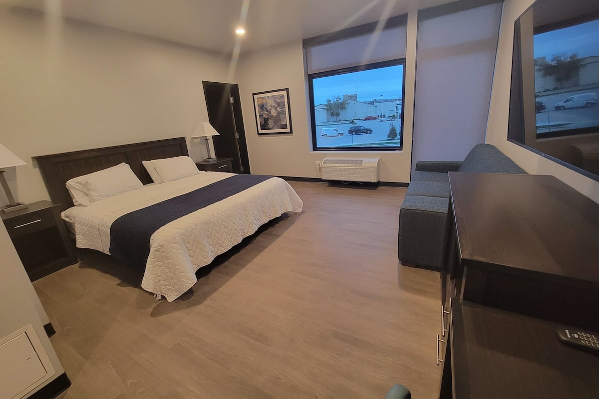 A hotel room with a bed, a desk, a chair, a window with a view of the street, and an air conditioning unit.