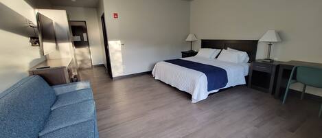 Habitación de hotel con cama, escritorio, silla, sofá y baño visible a través de una puerta abierta.