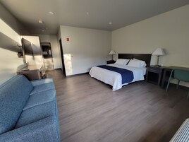 A hotel room with a bed, a desk, a chair, a sofa, and a bathroom visible through an open door.