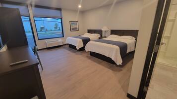 Habitación de hotel con dos camas, un escritorio con un control remoto, una ventana que da a la calle y una puerta que conduce a un área de ducha.