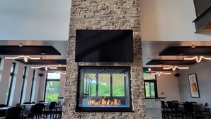 Een modern interieur met een stenen open haard, grote ramen en een flatscreen televisie erboven.