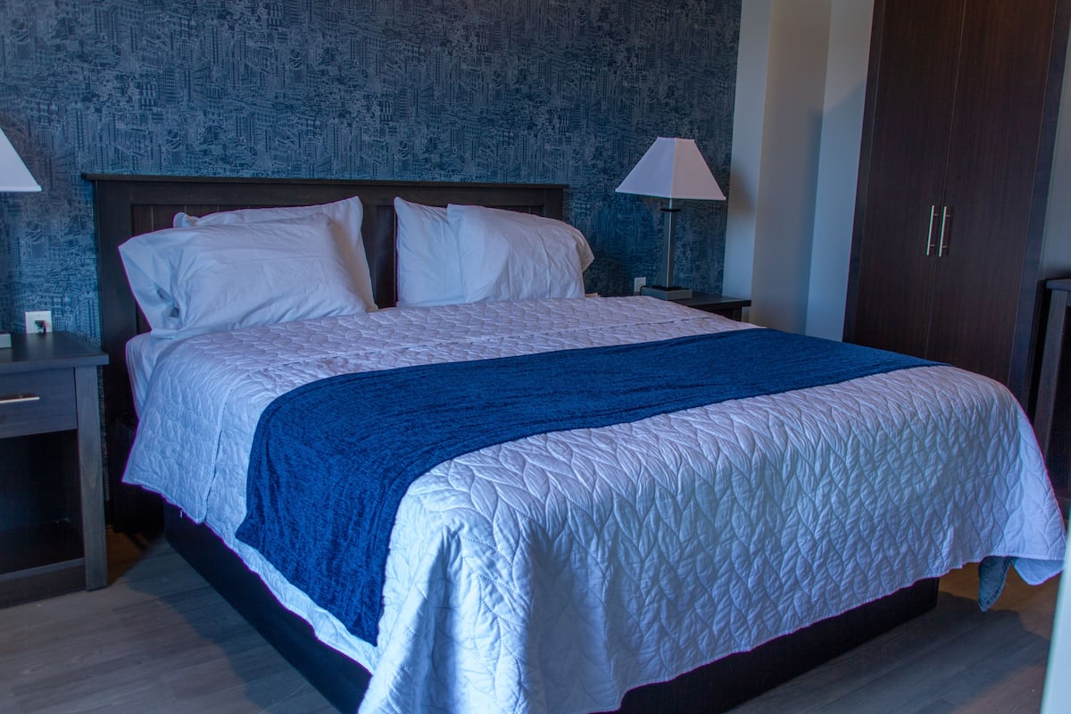A neatly made bed with white and blue bedding, a wooden headboard, and two bedside lamps.