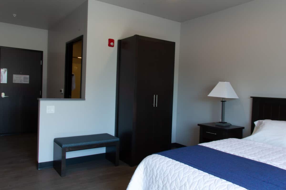 A hotel room with a bed, a bench, a wardrobe, a nightstand with a lamp, and a door.