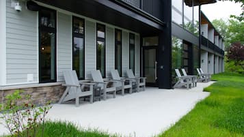 Un edificio moderno con una zona de estar al aire libre techada, con sillas y base de piedra.