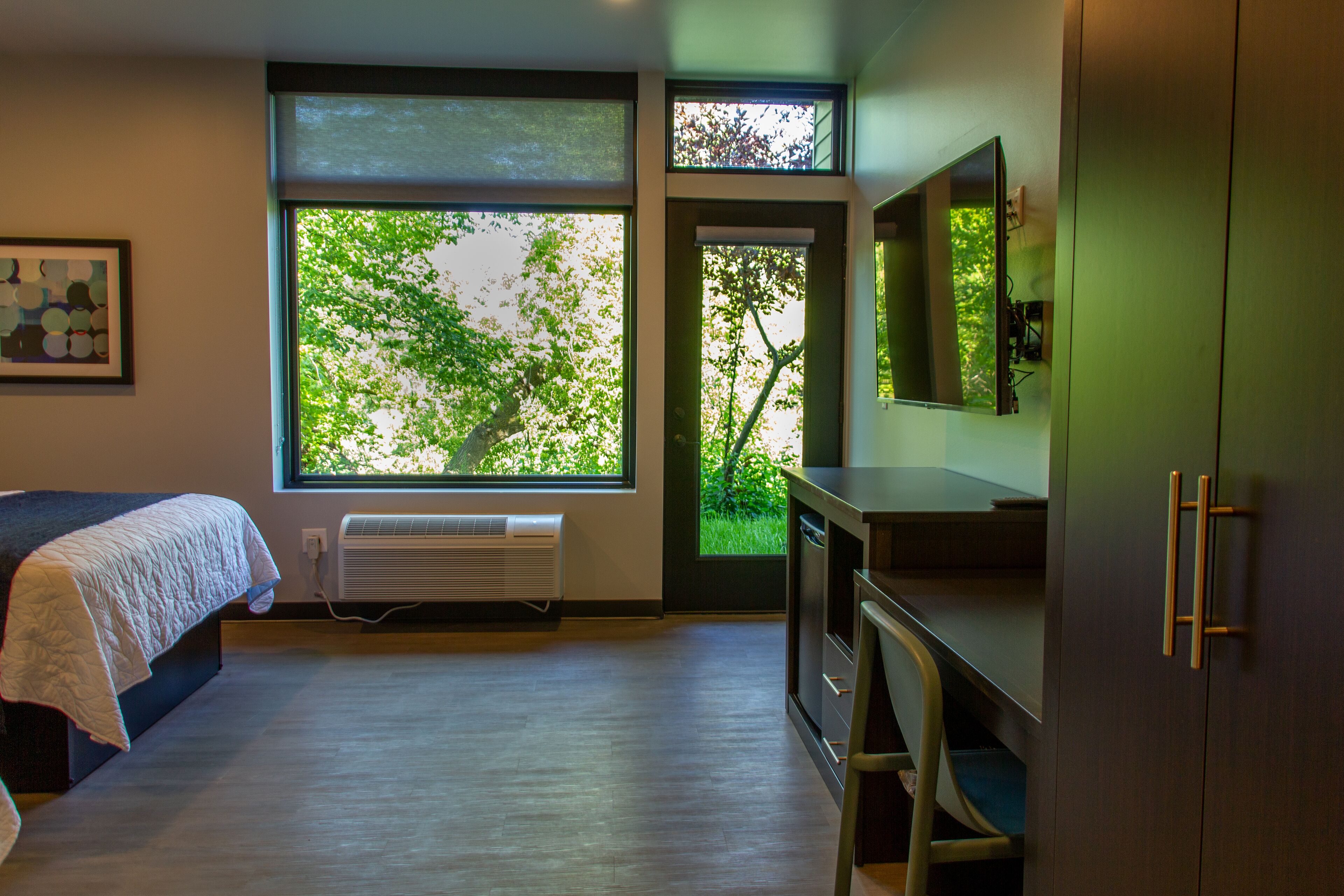 A bedroom with a bed, a large window with a view of trees, a radiator, and a wardrobe.