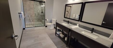 A modern bathroom with a shower, two sinks, and a large mirror.