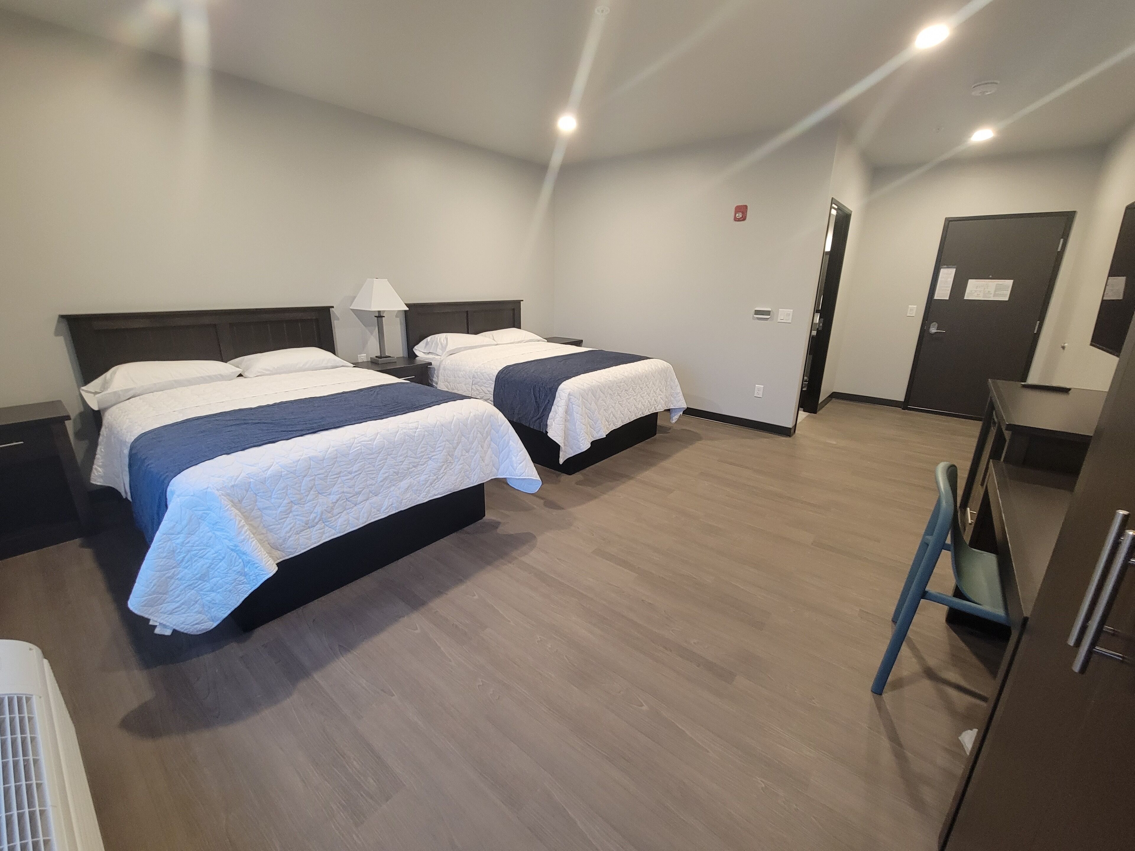 A hotel room with two beds, a desk, a chair, and a door.