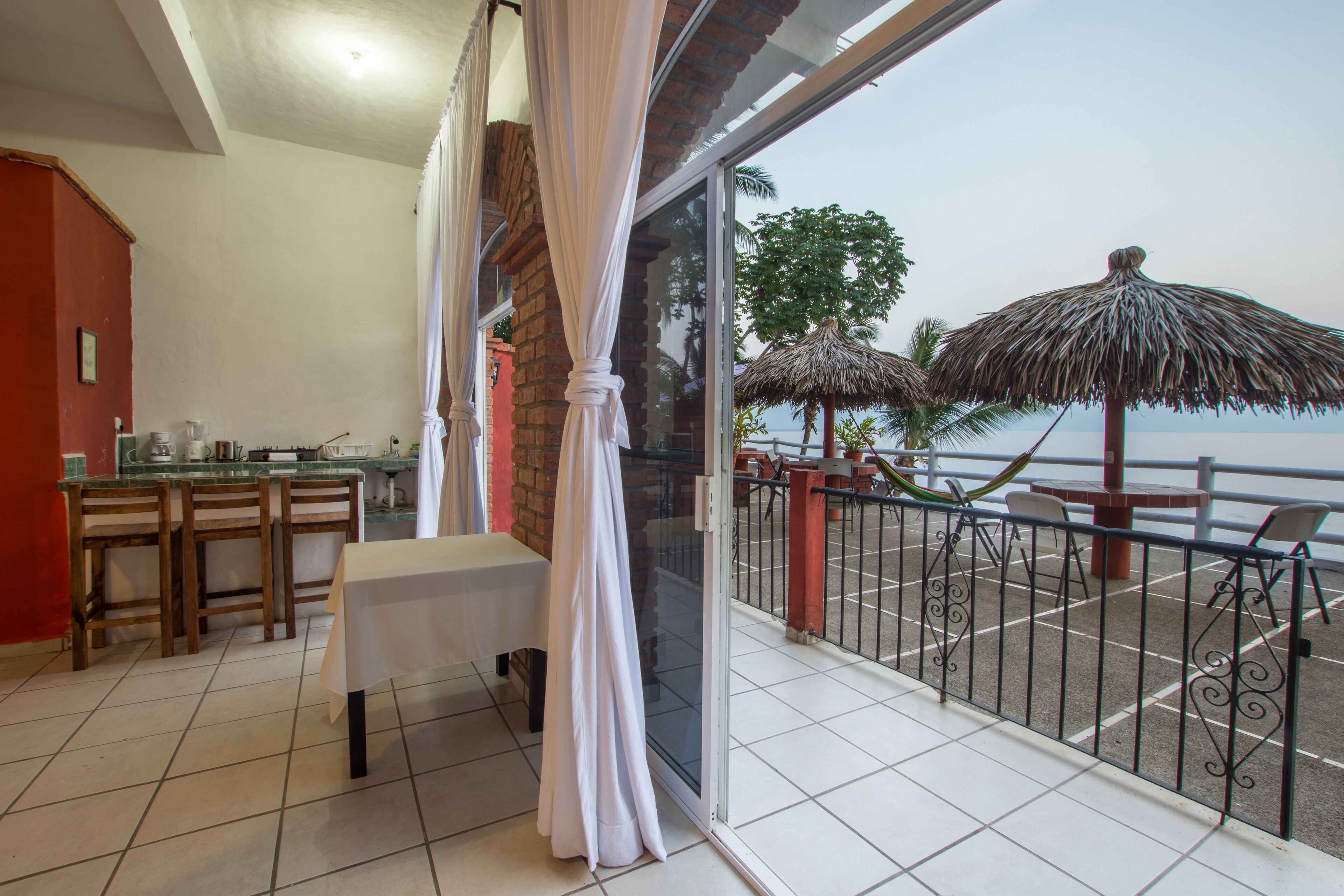 A balcony with a table and chairs, a view of the sea, and a thatched umbrella.
