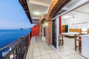 Een balkon met uitzicht op zee, een bed en een eethoek.