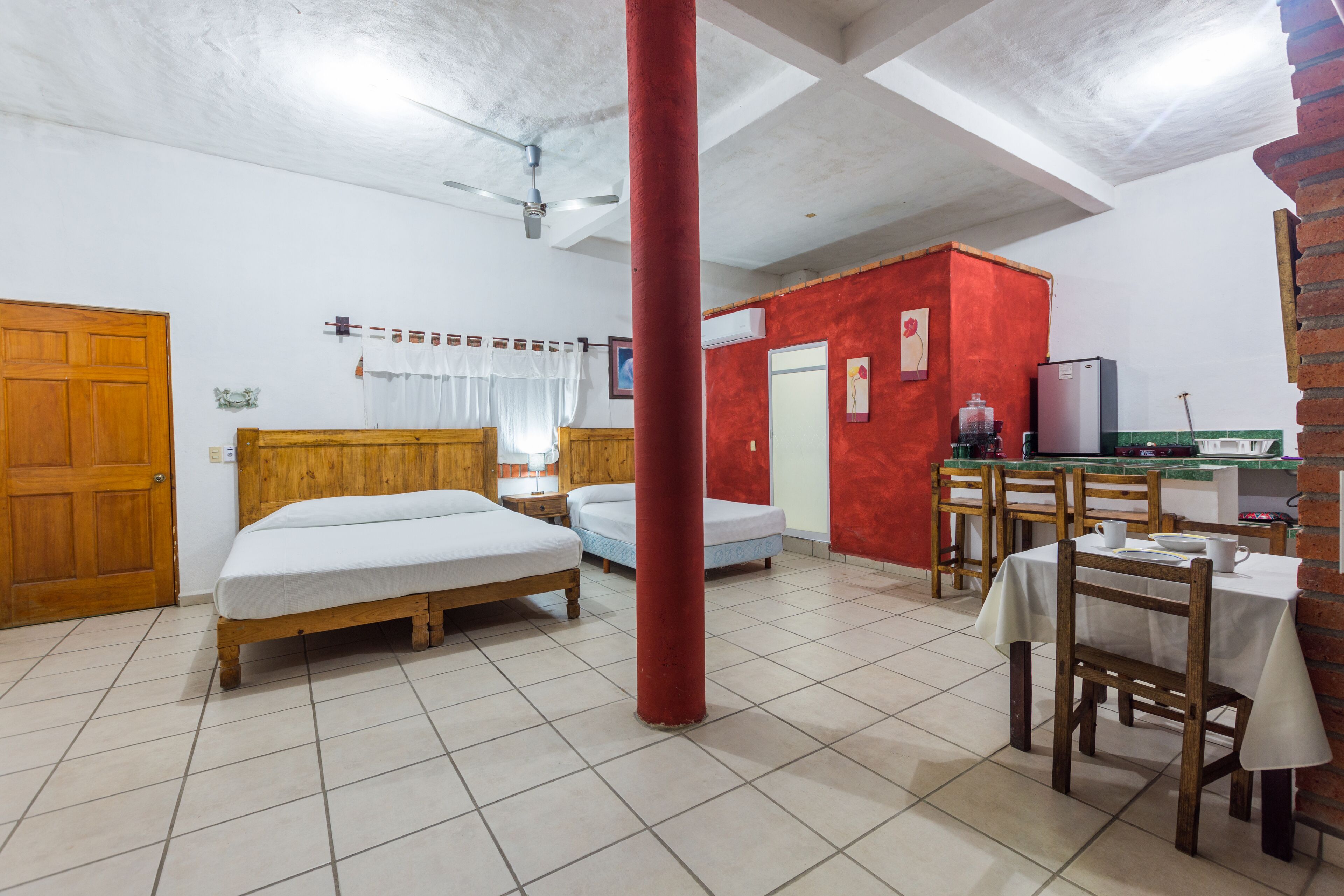 Een kamer met twee bedden, een eettafel met stoelen, een koelkast en een rode zuil.