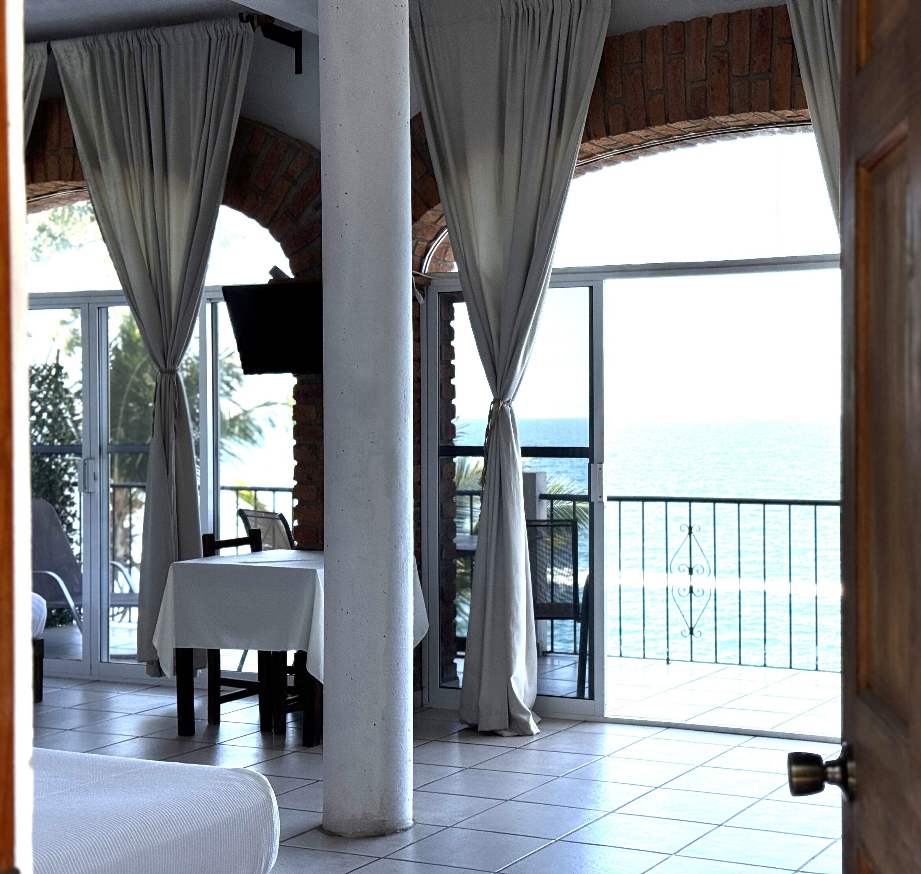 A balcony with a table and chairs, a view of the sea, and a brick wall.