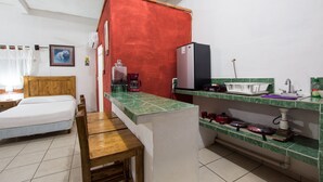 A compact kitchen with a bed, a wooden table, and a refrigerator. - Traditional Sierra Leon Oceanfront Rooms (Puerto Vallarta)