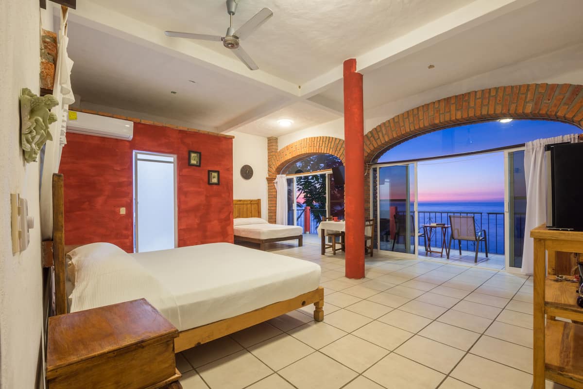Una habitación de hotel con cama, balcón con vistas, televisor y ventilador de techo.