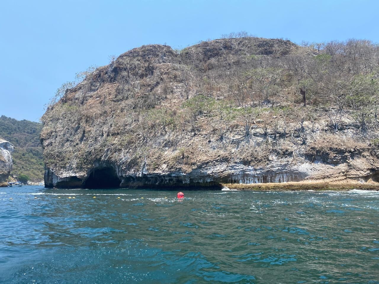 A coastal landscape with a rocky cliff and a cave entrance.