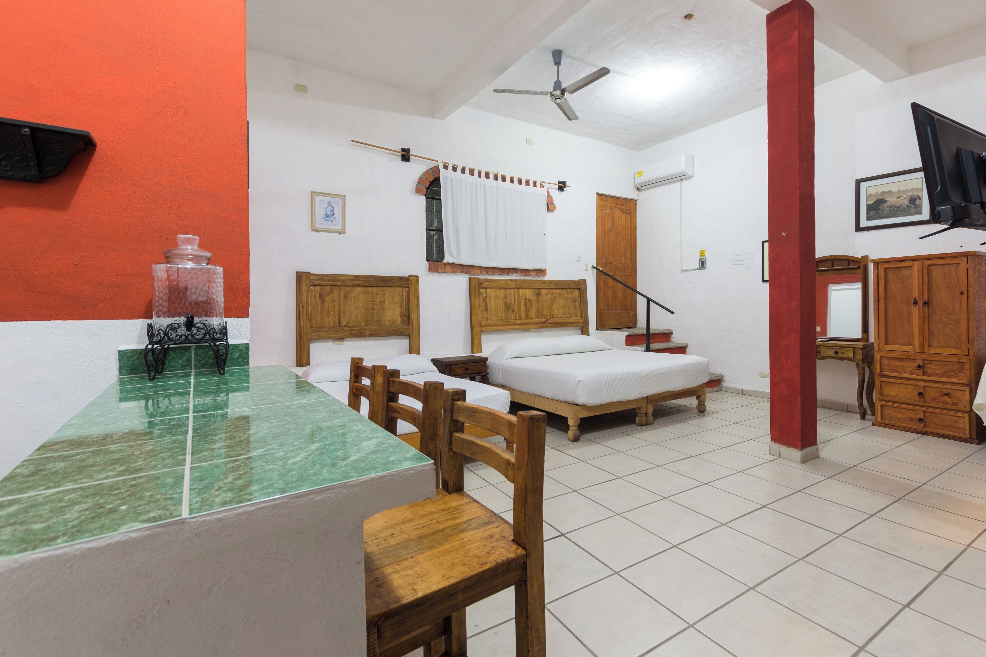 Habitación de hotel con una mesa de comedor, sillas de madera, dos camas, un armario y un ventilador de techo.