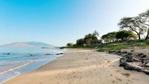 Una playa con cielos despejados, agua tranquila y una montaña distante.