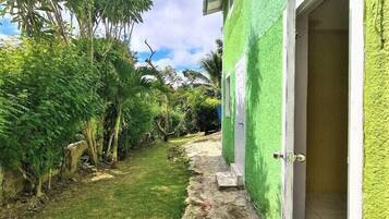 Un bâtiment vert avec une porte ouverte, un petit seuil menant à la porte et un chemin bordé d’herbe et de plantes.