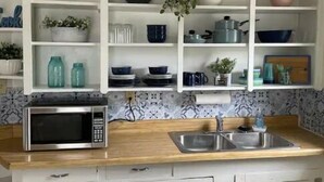 A kitchen with white cabinets, a microwave, a sink, and various dishes and utensils. - Fairy Bowery (Nauvoo)