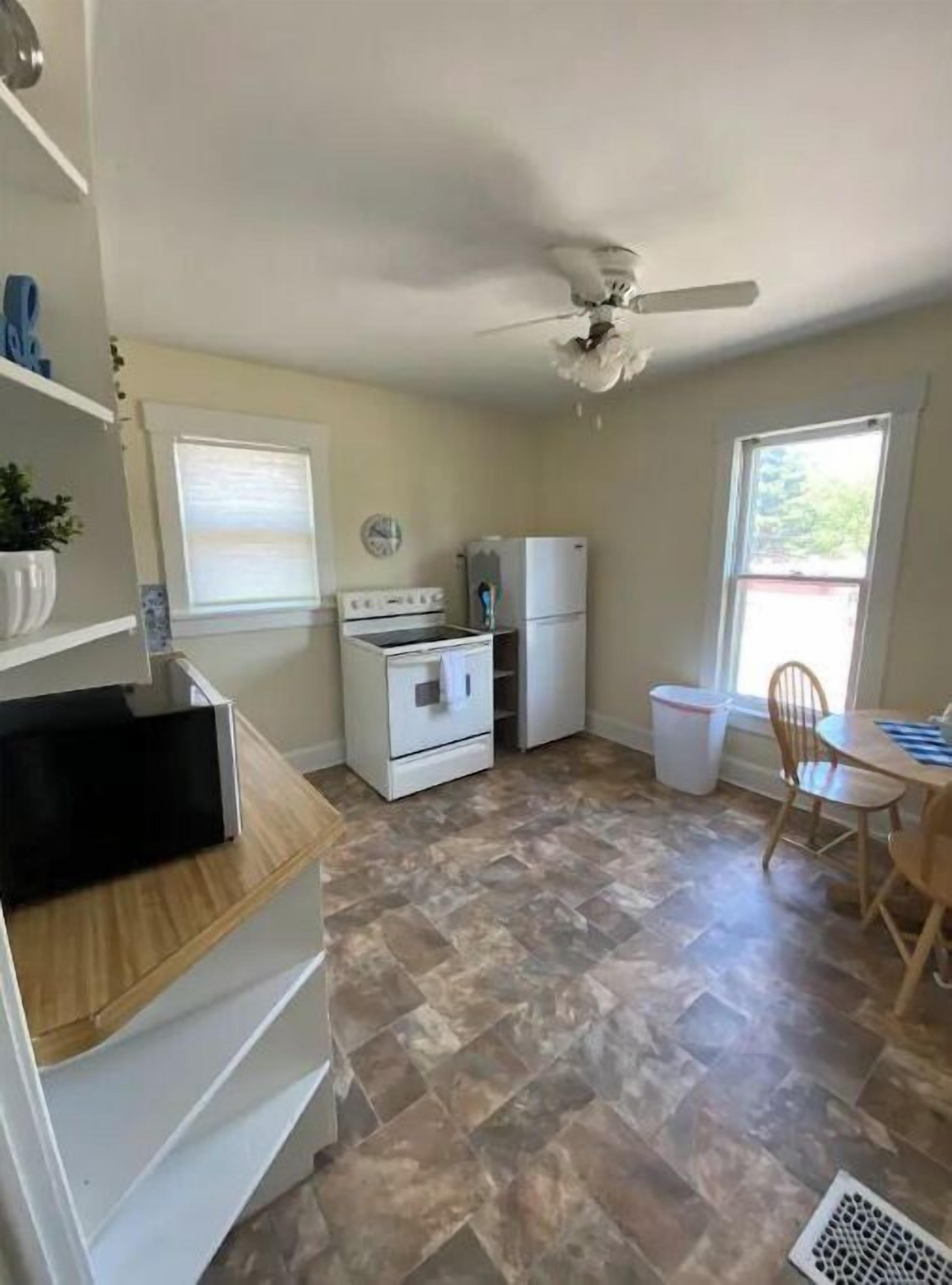 A compact kitchen with a stove, oven, and refrigerator, a dining table with chairs, and a ceiling fan.