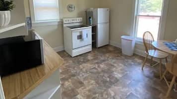 A compact kitchen with a stove, oven, and refrigerator, a dining table with chairs, and a ceiling fan.