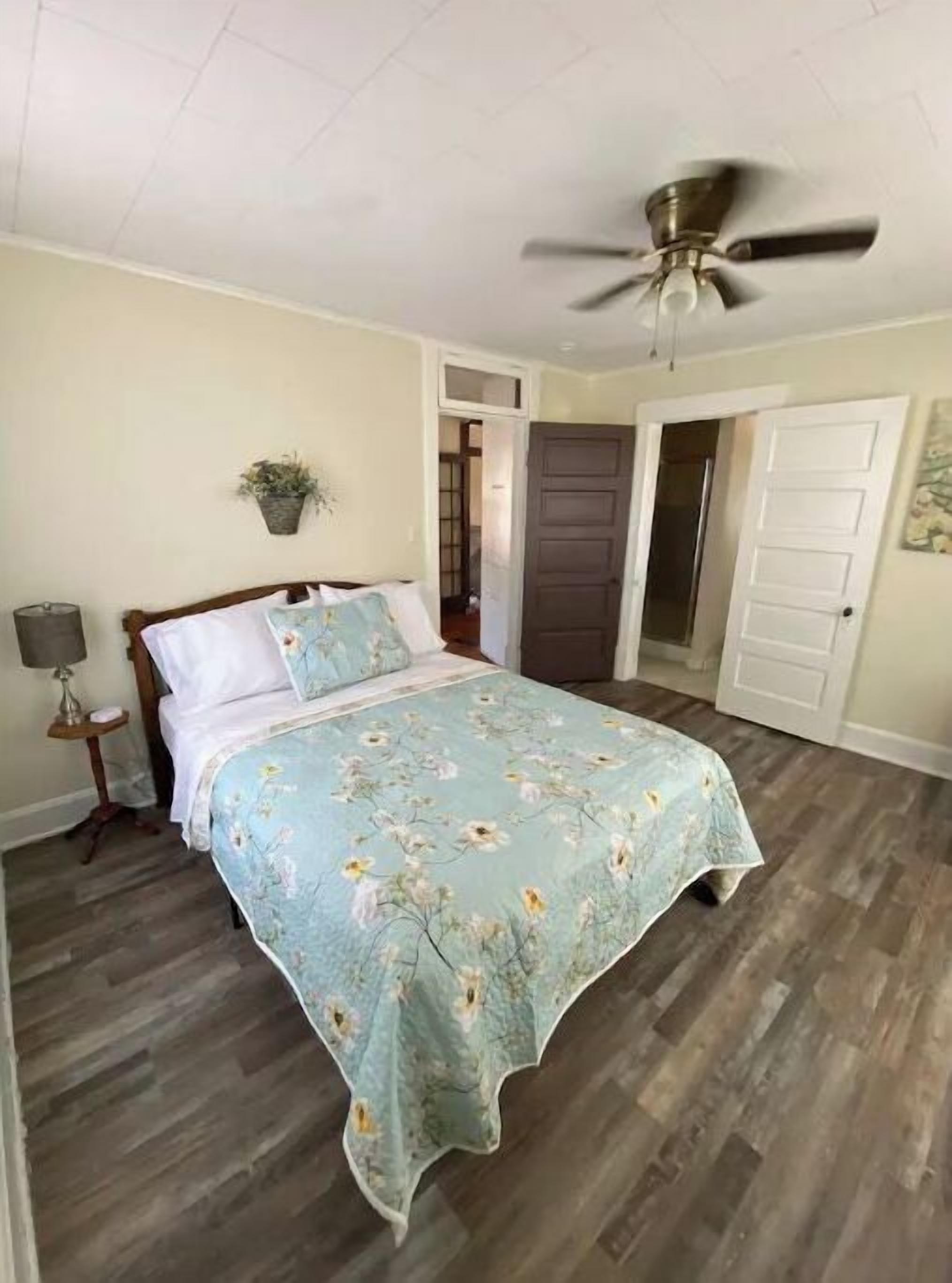 A bedroom with a bed, a ceiling fan, a nightstand, a lamp, and a door.