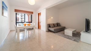 A modern living room with a sofa, coffee table, and TV. There is a dining area with a table and chairs. - Quarteira Beach - 2.º D by HelloVacations (Loulé)
