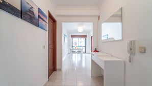 A hallway with a white sink and mirror, a wooden door, and a tiled floor. - Quarteira Beach - 2.º D by HelloVacations (Loulé)