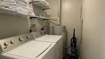 Un cuarto de lavandería con lavadora y secadora de carga frontal, un estante con toallas dobladas y una aspiradora.