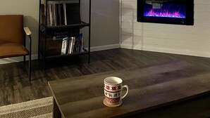 Un salon avec un téléviseur à écran plat fixé au-dessus d’une cheminée, une bibliothèque et une table basse sur laquelle se trouve une tasse.