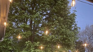 Une table et des chaises en bois, disposées sur une terrasse couverte et illuminée par des guirlandes lumineuses.