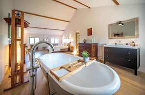 A modern bathroom with a freestanding bathtub, wooden floor, and a large mirror above the sink.