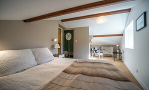 A bedroom with a bed, a desk, and a chair, a window, and a door leading to another room.